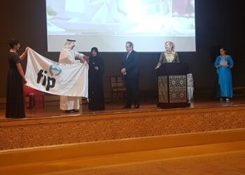 Jesús Aguilar recibe la bandera de la Federación Internacional Farmacéutica (FIP) , de su presidente, Dominique Jordan, y de la presidenta de los farmacéuticos de Emiratos Árabes Mariam Galadari