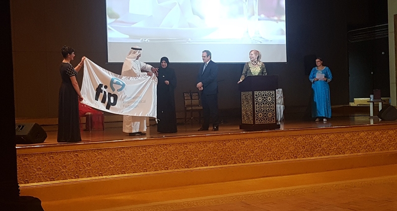 Jesús Aguilar recibe la bandera de la Federación Internacional Farmacéutica (FIP) , de su presidente, Dominique Jordan, y de la presidenta de los farmacéuticos de Emiratos Árabes Mariam Galadari